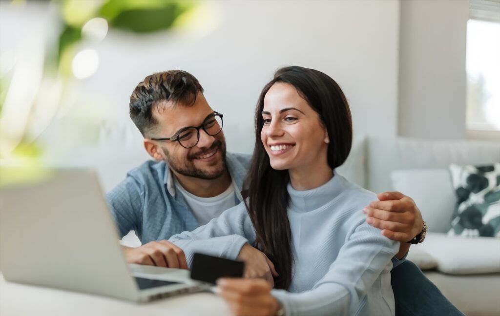 Una pareja feliz y sonriente revisando sus finanzas juntos, demostrando la importancia de abordar el tema de parejas y finanzas de forma conjunta y armoniosa.
